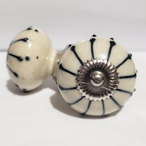 May include: Two white ceramic cabinet knobs with black and silver accents. The knob on the right has a silver center with a black and white striped design. The knob on the left has a black and white speckled design.