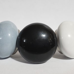 May include: Three ceramic knobs in a row. The knob on the left is light blue, the middle knob is black, and the knob on the right is white.