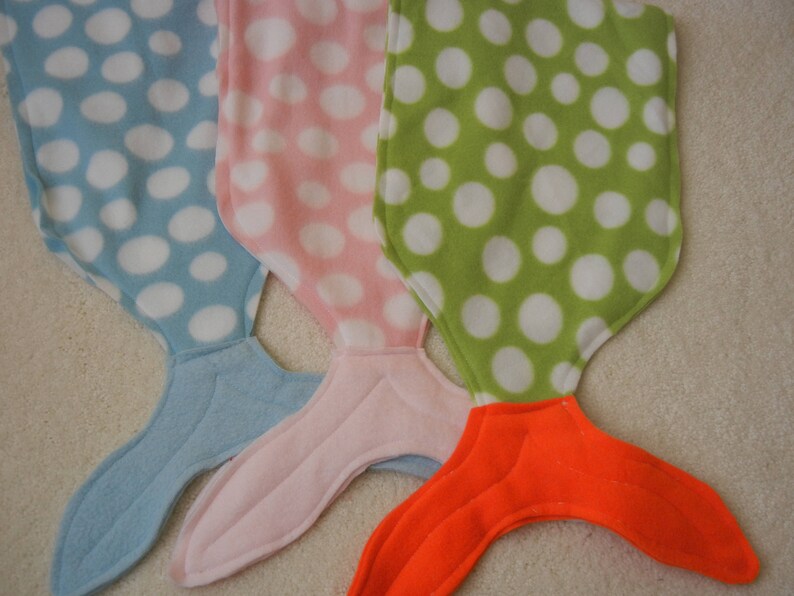 Image of doll mermaid tails: blue/white polka dot  with light blue tail;  pink/white polka dot  with pink tail;  and  green/white polka dot  with orange tail;