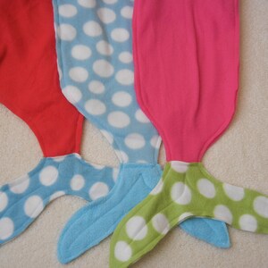 Image of doll mermaid tails: red with blue/white polka dot tail ;  pink/white polka dot  with pink tail;  and  pink with green/white tail
