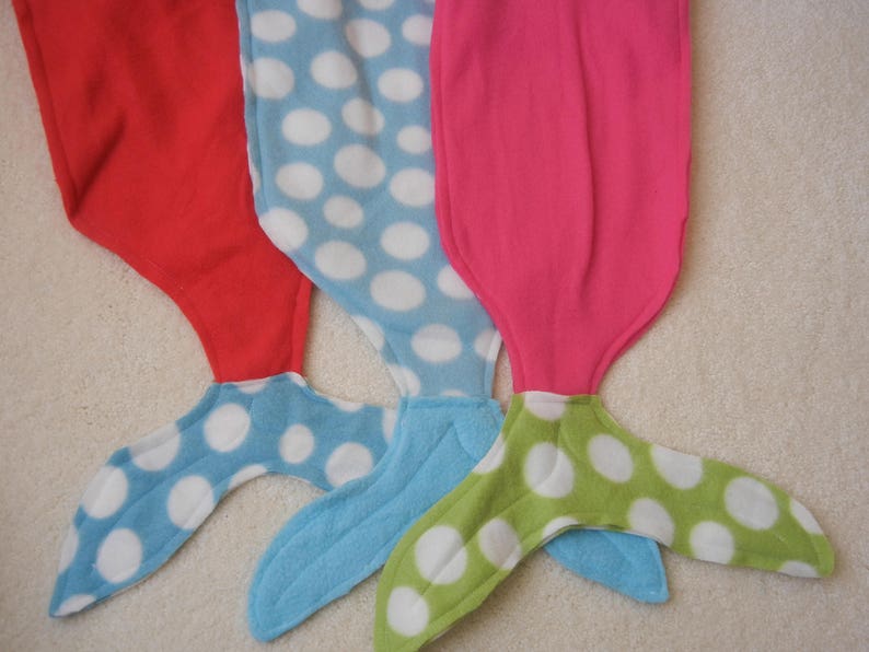 Image of doll mermaid tails: red with blue/white polka dot tail ;  pink/white polka dot  with pink tail;  and  pink with green/white tail