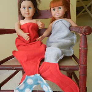 Image of dolls wearing  mermaid tails:   red with blue/white polka dot tail and pale  blue  with red tail