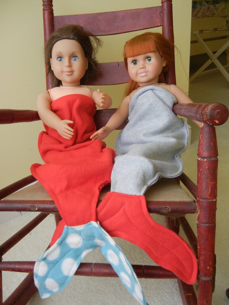 Image of dolls wearing  mermaid tails:   red with blue/white polka dot tail and pale  blue  with red tail