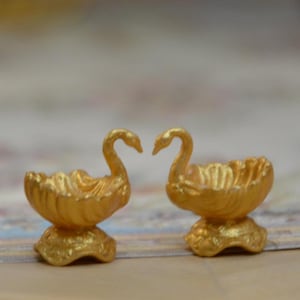May include: A silver thimble and two small gold swan-shaped decorative bowls. The thimble is textured with small dimples. The swans have curved necks and sit on pedestal bases, with their heads touching.