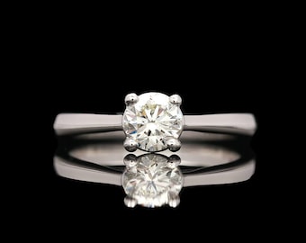 May include: A silver solitaire engagement ring with a round brilliant cut diamond.