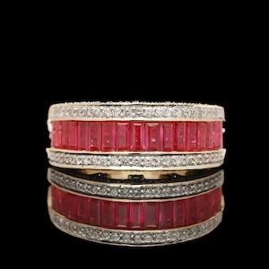May include: A luxurious ring featuring a band of vibrant red gemstones, likely rubies, set between rows of sparkling white diamonds. The ring's design is bold and eye-catching, with a polished gold band. The ring is displayed against a black background.