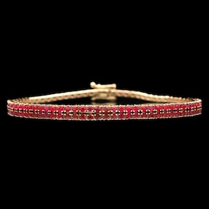 May include: A gold bracelet with two rows of small, vibrant red gemstones. The bracelet has a secure clasp and is set against a black background, highlighting the jewelry's sparkle and design. A classic piece of jewelry.