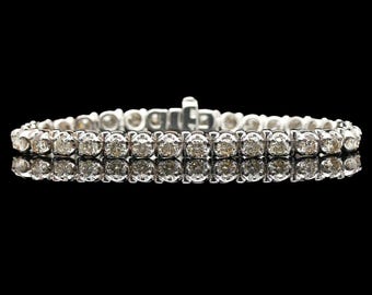 May include: A silver bracelet with two rows of round, clear diamonds. The bracelet is set against a black background, with a reflection of the bracelet visible below. The clasp is visible at the top.
