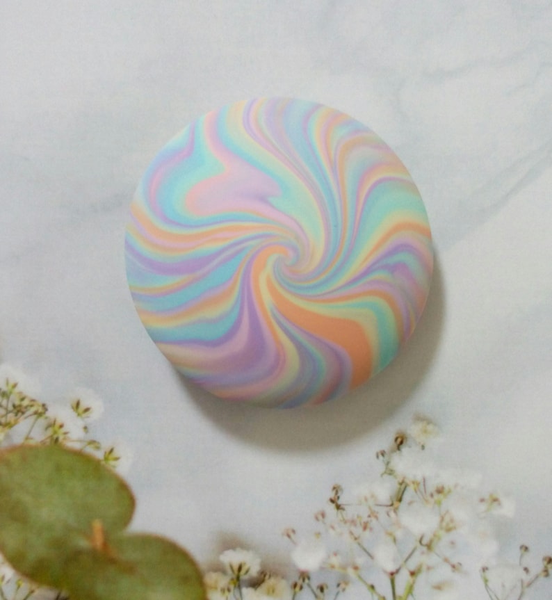 May include: A circular, flat object featuring a swirling, marbled pattern of pastel colors including light blue, soft pink, lavender, and peach. The design radiates from the center in a continuous, smooth, and blended spiral motion.