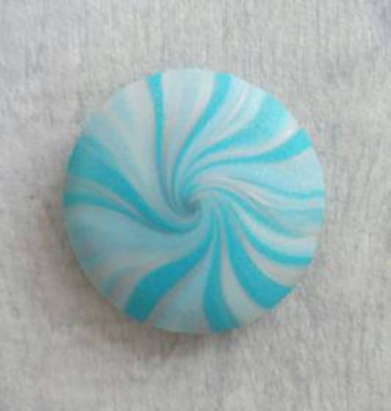 May include: A circular button featuring a swirling pattern of bright turquoise and white colors. The design radiates from the center outward in a spiral motion, creating a smooth, rounded surface with a consistent color distribution throughout.