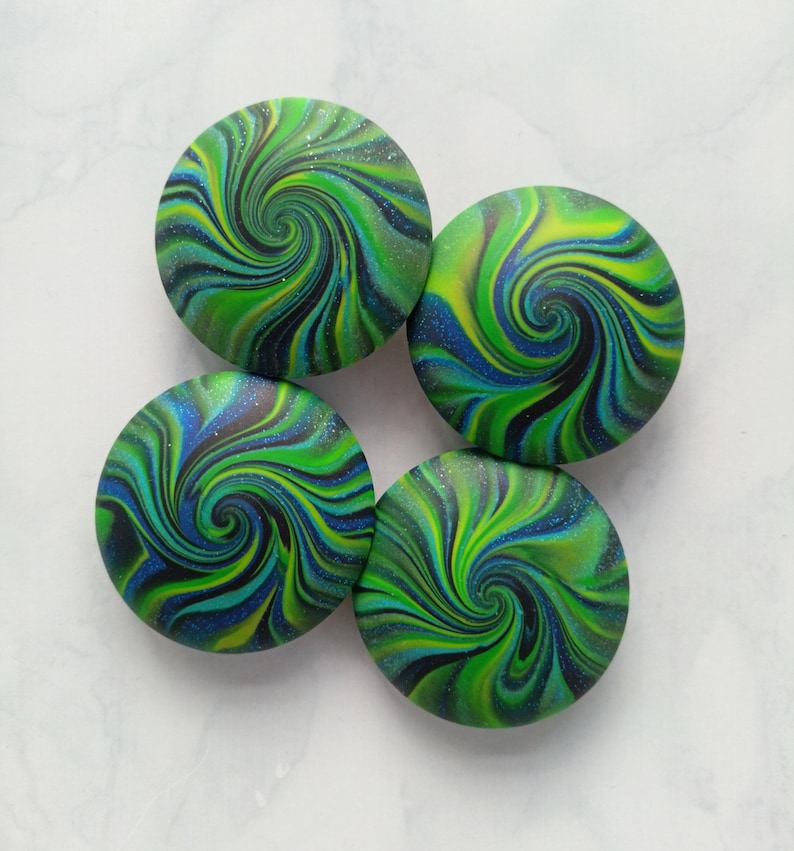 May include: Four circular buttons featuring a swirling marbled pattern in shades of lime green, deep blue, and black. Each button has a smooth, glossy finish with fine glitter particles embedded throughout the surface, creating a vibrant, multi-colored effect.