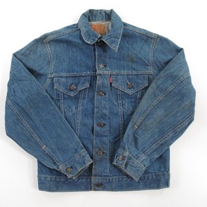 May include: A vintage blue denim jacket with a button closure, two front pockets, and a single pocket on the left chest. The jacket has a faded look and shows signs of wear.