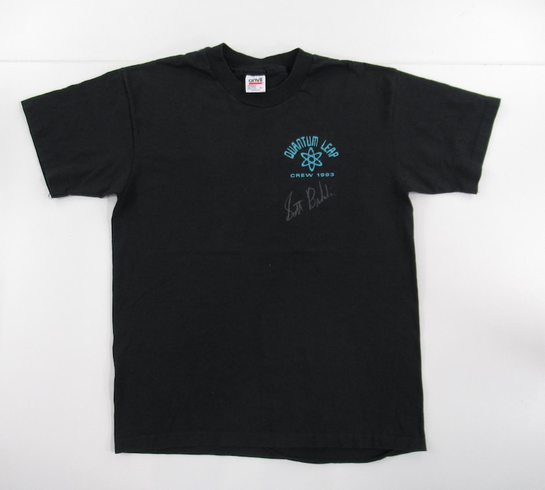 Puede incluir: Camiseta negra con un logotipo de Quantum Leap azul y blanco y el texto "Crew 1993". La camiseta est&aacute; firmada por "Scott Bakula".