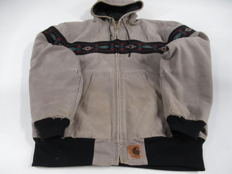 May include: A gray hooded jacket with a black and brown patterned band across the chest. The jacket has a zipper closure and a Carhartt logo patch on the bottom right side.