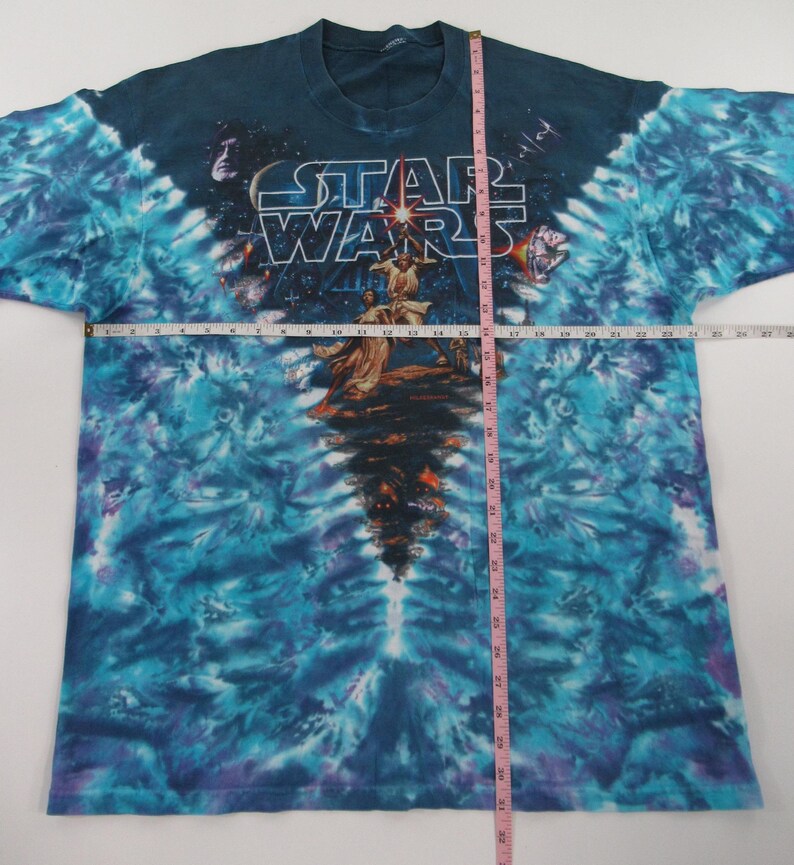 Puede incluir: Una camiseta tie-dye azul, morado y blanco con un gr&aacute;fico de Star Wars. El gr&aacute;fico presenta a Luke Skywalker, Darth Vader y el Halc&oacute;n Milenario. El texto "Star Wars" est&aacute; impreso en blanco.