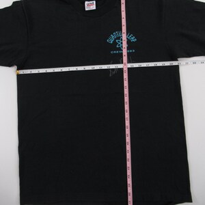 Puede incluir: Camiseta negra con un logotipo de Quantum Leap azul y blanco y el texto "Crew '93". La camiseta se mide con una cinta m&eacute;trica rosa.