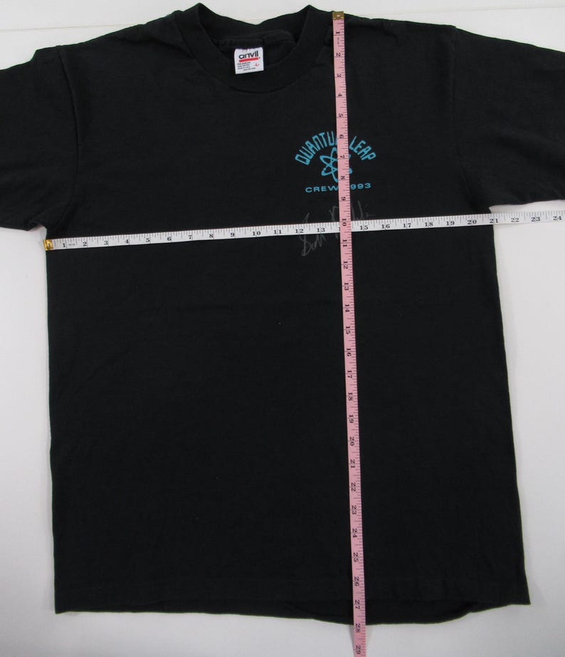 Puede incluir: Camiseta negra con un logotipo de Quantum Leap azul y blanco y el texto "Crew '93". La camiseta se mide con una cinta m&eacute;trica rosa.