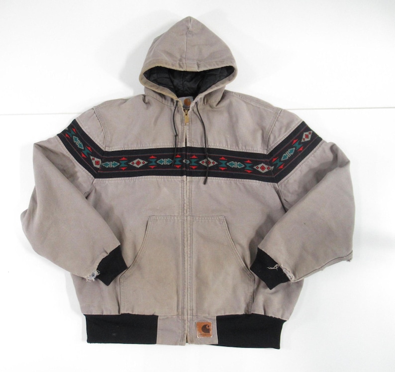 May include: A gray hooded jacket with a black zipper and a black and brown patterned band across the chest. The jacket has a Carhartt logo on the bottom left side.