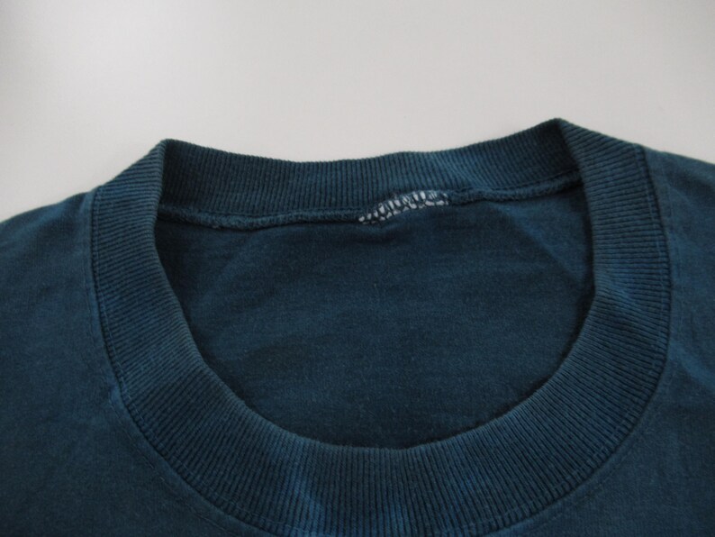 Puede incluir: Primer plano del cuello de una camiseta de color azul oscuro. El cuello es redondo y tiene una textura acanalada.