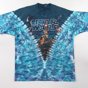 May include: A tie-dye t-shirt with a blue, purple, and white color scheme. The shirt features a graphic of the Star Wars characters Luke Skywalker and Darth Vader with the text "STAR WARS" above them.
