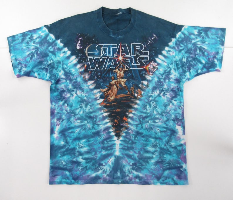 Puede incluir: Una camiseta tie-dye con un esquema de color azul, morado y blanco. La camiseta presenta un gr&aacute;fico de los personajes de Star Wars Luke Skywalker y Darth Vader con el texto "STAR WARS" encima.
