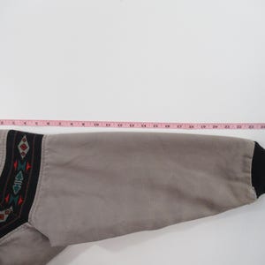 May include: A gray jacket with a black and brown geometric pattern on the sleeve. The sleeve is rolled up and the cuff is black.