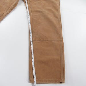 Puede incluir: Un pantal&oacute;n de trabajo marr&oacute;n con una cinta m&eacute;trica que muestra una longitud de entrepierna de 81 cm.