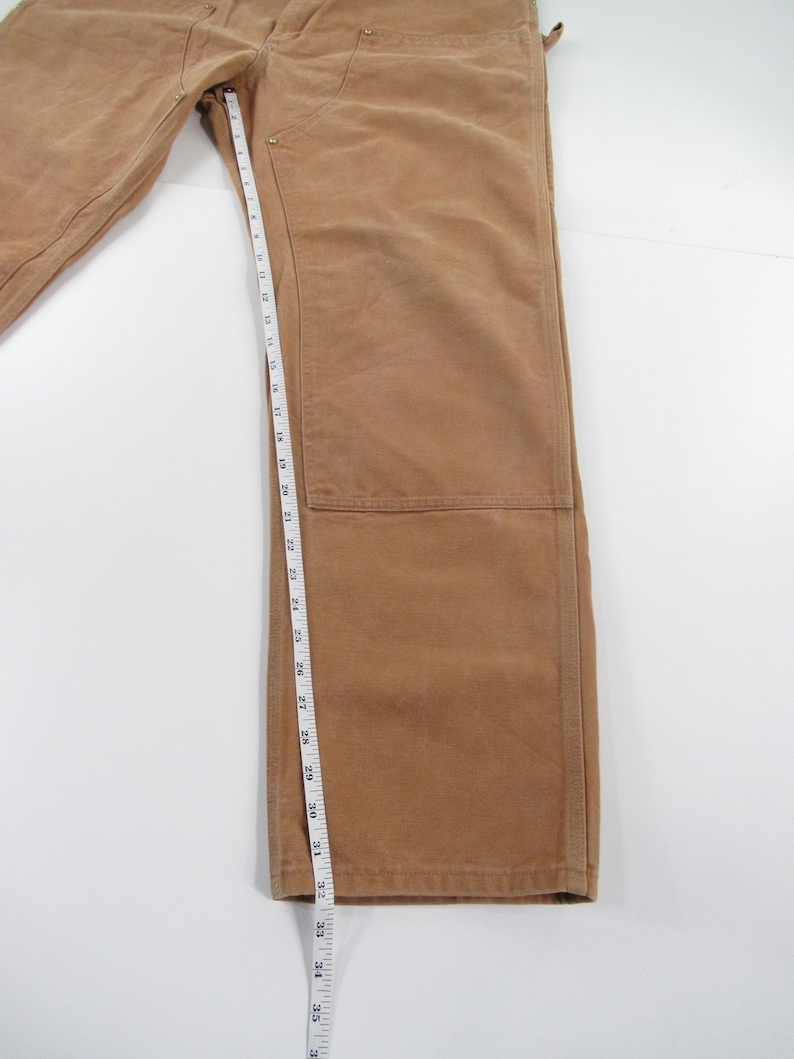 Puede incluir: Un pantal&oacute;n de trabajo marr&oacute;n con una cinta m&eacute;trica que muestra una longitud de entrepierna de 81 cm.