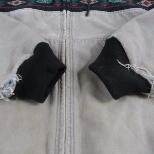 May include: A gray zip-up jacket with black ribbed cuffs. The jacket has a geometric pattern in black, red, green, and blue across the top.