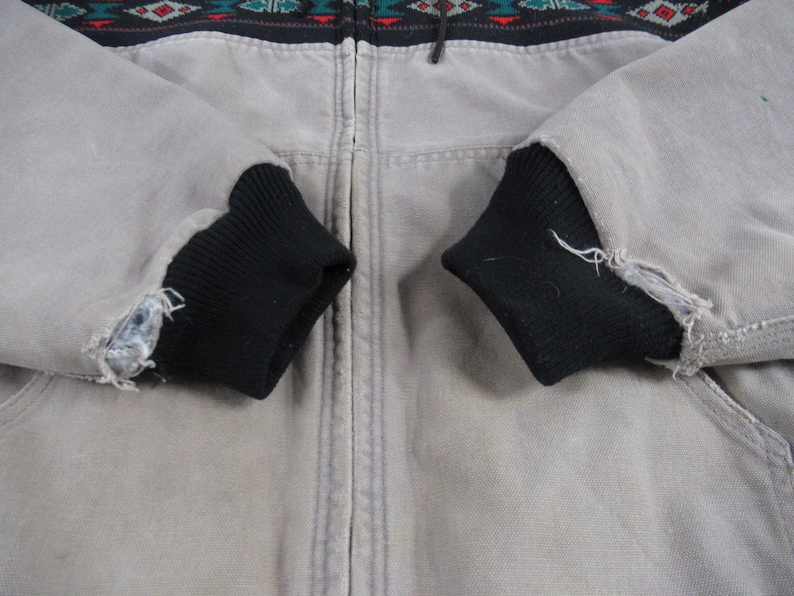 May include: A gray zip-up jacket with black ribbed cuffs. The jacket has a geometric pattern in black, red, green, and blue across the top.