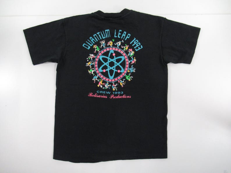 Puede incluir: Camiseta negra con un gr&aacute;fico colorido de un c&iacute;rculo con un s&iacute;mbolo de &aacute;tomo en su interior y el texto "Quantum Leap 1993" encima. El texto "Crew 1993 Belisarius Productions" est&aacute; debajo del c&iacute;rculo.