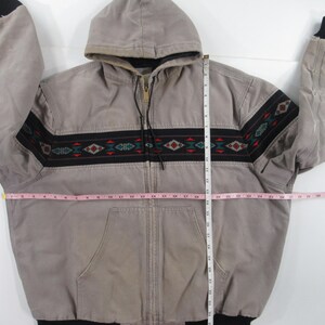 May include: A gray hooded Carhartt jacket with a black and red patterned band around the waist. The jacket has a zipper closure and a black Carhartt logo patch on the bottom right side.