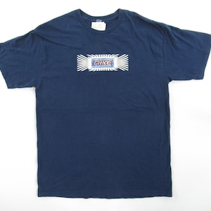 Op de afbeelding: Een donkerblauw t-shirt met een witte en blauwe afbeelding van het Nike-logo met de tekst "Nike" in rood en wit.