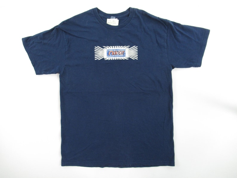 Op de afbeelding: Een donkerblauw t-shirt met een witte en blauwe afbeelding van het Nike-logo met de tekst "Nike" in rood en wit.