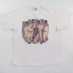 May include: White t-shirt with a printed image of the band Boyz II Men. The band members are wearing white suits and are standing in a group. The text "Boyz II Men" is printed in blue letters.