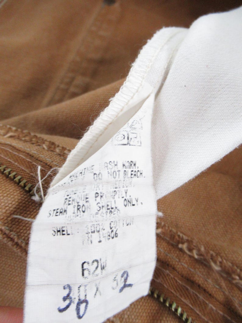 Puede incluir: Una etiqueta de cuidado blanca con texto negro unida a una tela marr&oacute;n. La etiqueta dice "NO BLANQUEAR.  ENJUAGAR INMEDIATAMENTE. PLANCHAR A VAPOR SOLO LA CAPA, CAPA: 100% ALGOD&Oacute;N TN14806 62W 38 x 32"
