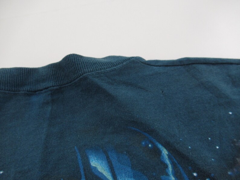 Puede incluir: Una camiseta azul oscuro con un dise&ntilde;o abstracto descolorido. El dise&ntilde;o parece ser una galaxia o nebulosa con estrellas y colores que se arremolinan.