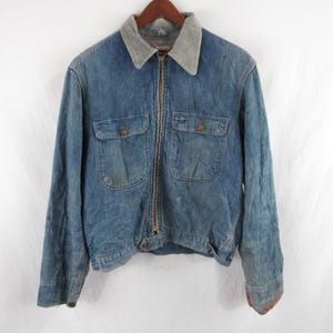May include: A vintage blue denim jacket with a gray corduroy collar, two chest pockets, and a full zipper closure. The jacket has a worn appearance, with visible wear and tear, and is hanging on a wooden hanger.