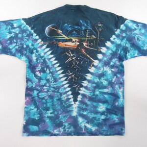 Puede incluir: Una camiseta tie-dye azul, morado y blanco con una imagen de Star Wars en la espalda. La imagen muestra a Darth Vader y cazas X-Wing en el espacio.