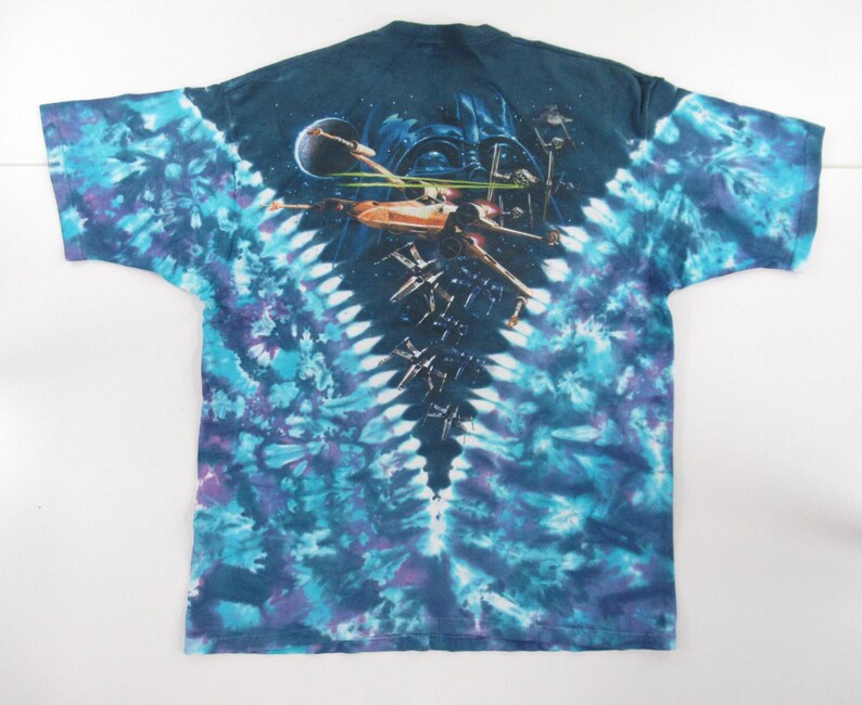 Puede incluir: Una camiseta tie-dye azul, morado y blanco con una imagen de Star Wars en la espalda. La imagen muestra a Darth Vader y cazas X-Wing en el espacio.