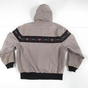 May include: A gray hooded jacket with a black and brown geometric pattern around the waist. The jacket has a black drawstring hood and a black elastic waistband.