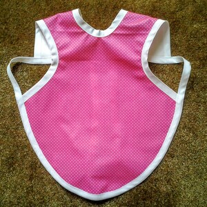May include: Pink and white polka dot bib with white trim. The bib has a neck opening and two straps that tie at the back.