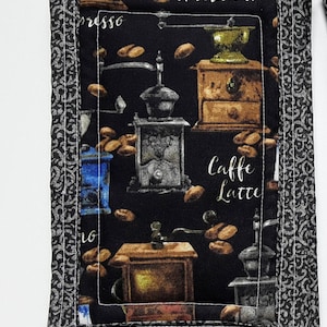 May include: Black fabric pot holder with a white stitched border. The fabric features a vintage coffee grinder design with the words "presso" and "caffe latte".