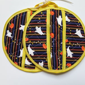 May include: Two black and yellow striped pot holders with a Halloween theme. The pot holders feature white ghosts and orange pumpkins on a black background. The pot holders have a yellow trim.