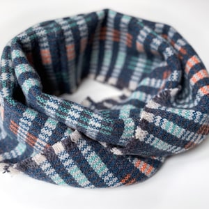 Könnte beinhalten: Ein blauer, grüner und orangefarbener karierter Schal. Der Schal ist zu einem Kreis gefaltet und liegt auf einer weißen Oberfläche.