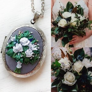 May include: A silver locket with a gray background and an embroidered bouquet of white flowers with green leaves. The locket is hanging from a silver chain.
