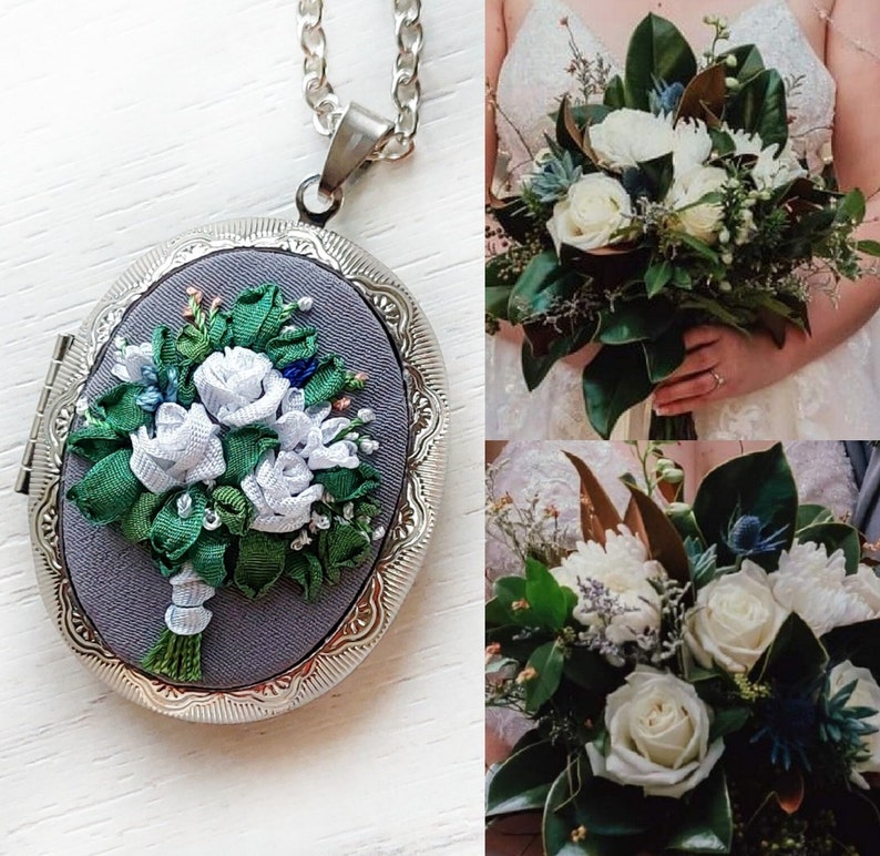 May include: A silver locket with a gray background and an embroidered bouquet of white flowers with green leaves. The locket is hanging from a silver chain.