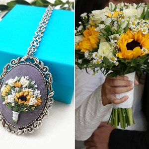 May include: A silver necklace with a round pendant featuring an embroidered bouquet of white and yellow flowers, including sunflowers, on a gray background.