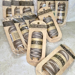 May include: Multiple spools of Darice 20lb 100% natural hemp cord packaged in individual brown cardboard cards. Each spool contains 205 feet of multi-toned brown, tan, and white twisted fiber cord, clearly labeled with the brand and length.