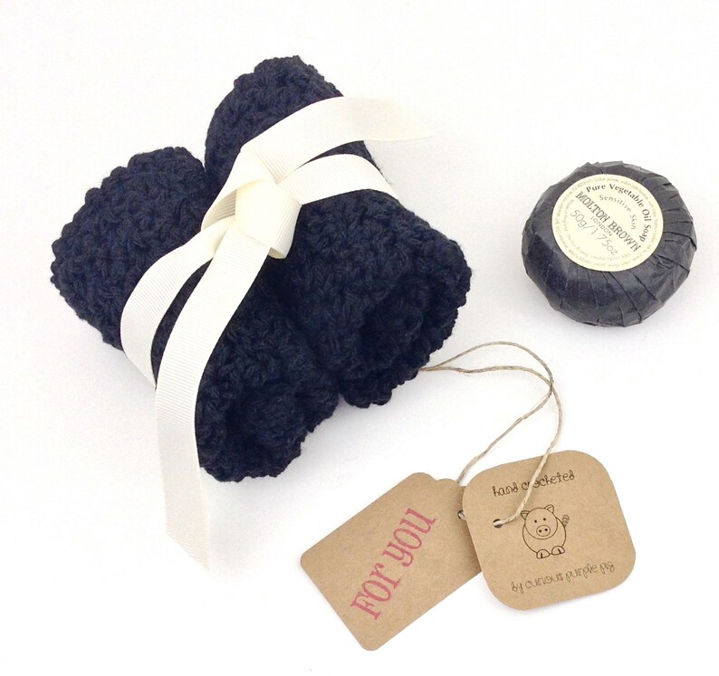 May include: A gift set with a black washcloth, a black bar of soap, and a brown gift tag that says "For You". The soap is wrapped in black paper and has a white label that says "Molton Brown" and "Pure Vegetable Oil Soap".